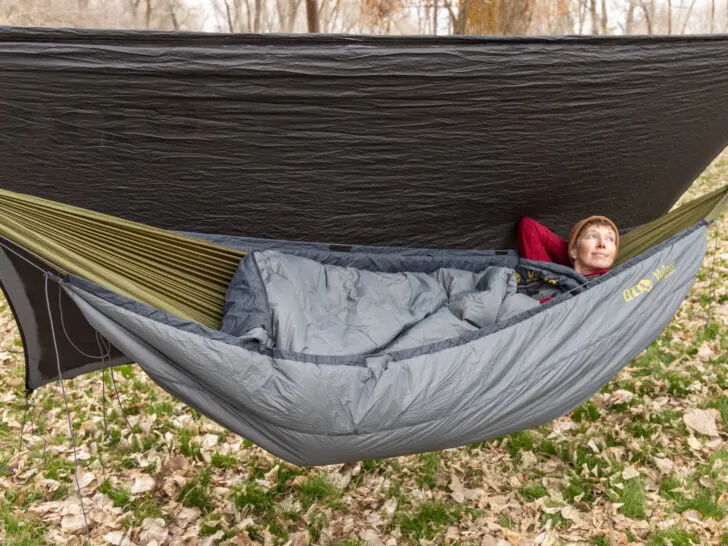 A woman relaxes in a camping hammock with underquilt and tarp.